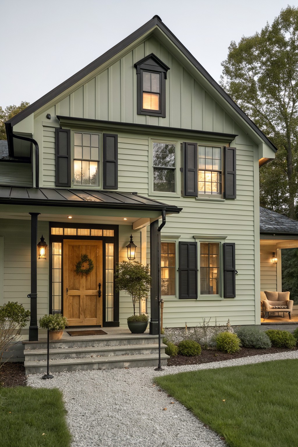 A two-story house with light green siding, black shutters and trim, a wooden front door, and a gravel path leading to concrete steps.