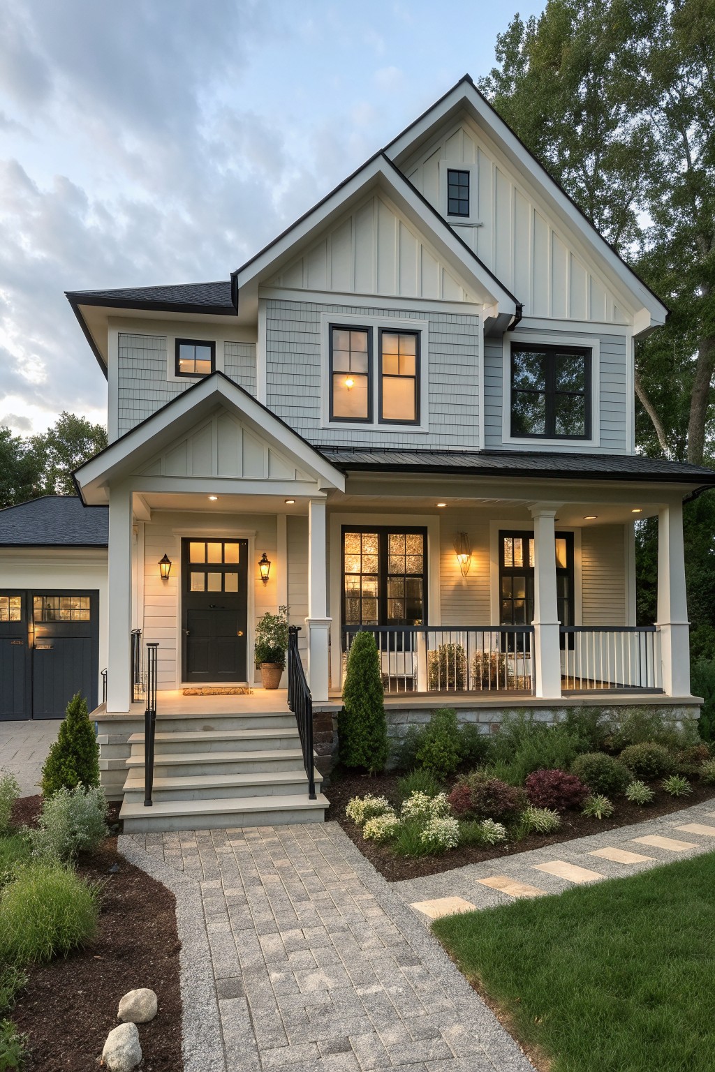 A two-story house with white vertical siding on the upper facade, gray shingles on the lower level, a wide front porch with white columns, and a paved walkway leading to the entrance.