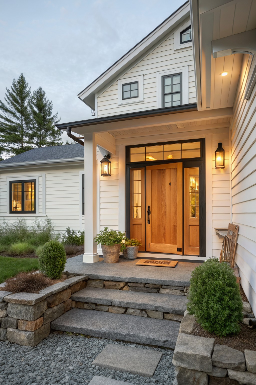 A white farmhouse exterior featuring a large natural wood front door with black trim, stone steps, and two wall lanterns.