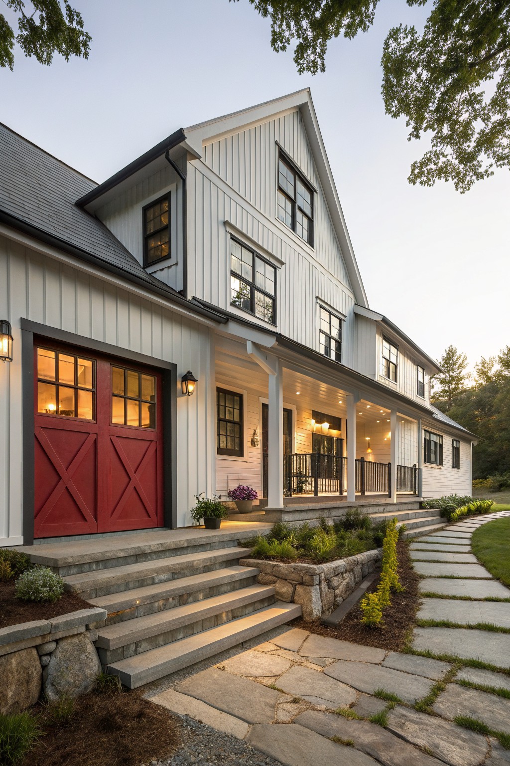 White farmhouse with red barn doors, lit porch, stone steps, and pathway at dusk