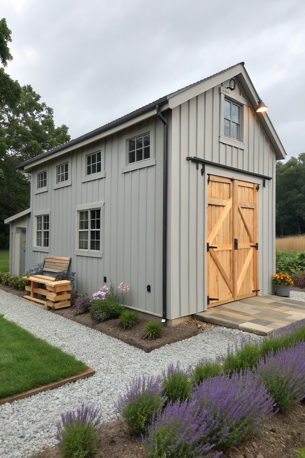 Gray barn with wooden doors amid purple flowers and gravel garden path
