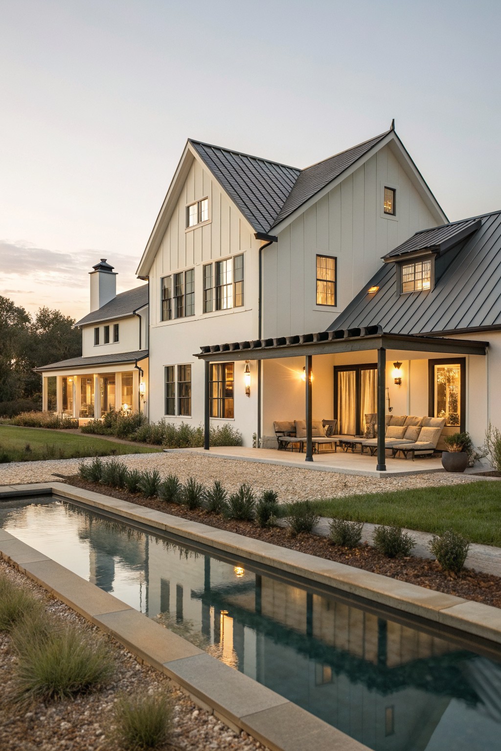 A white modern barn-style house with dark metal roofing, multiple gables, and a covered patio next to a long rectangular pool.