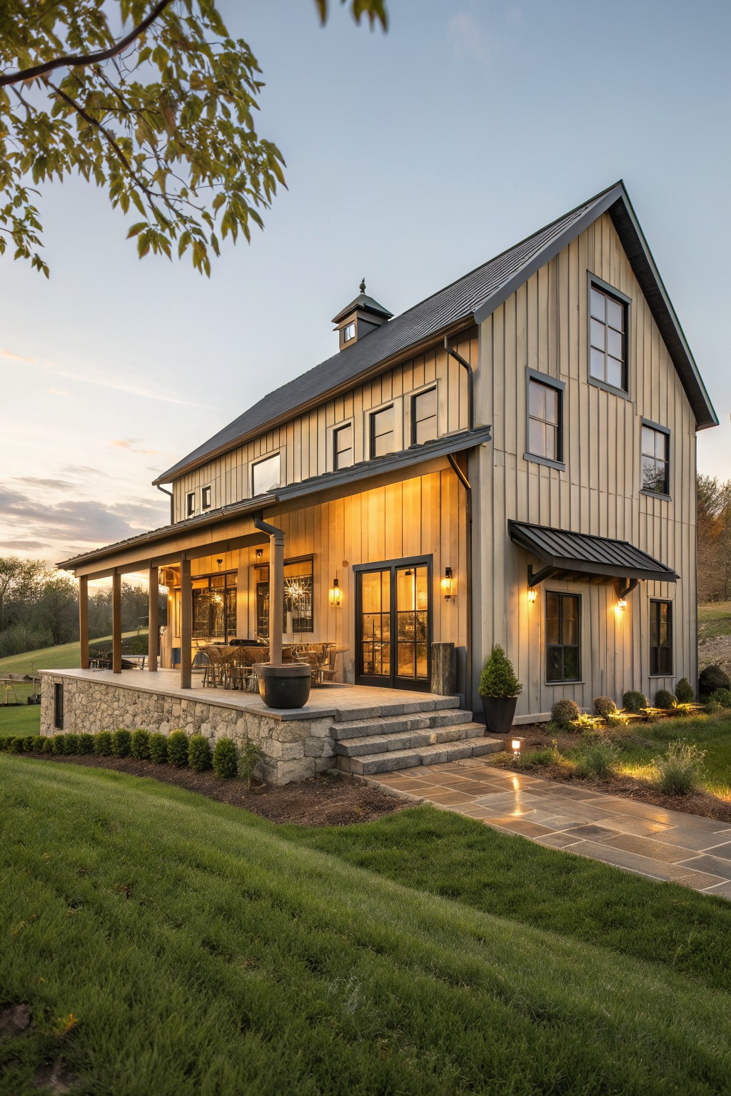 Modern two-story barn house with illuminated porch and stone steps at dusk