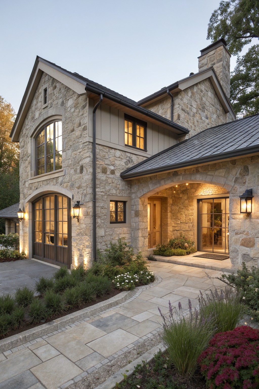 Stone house with arched windows and doorways glowing amid landscaped gardens at dusk