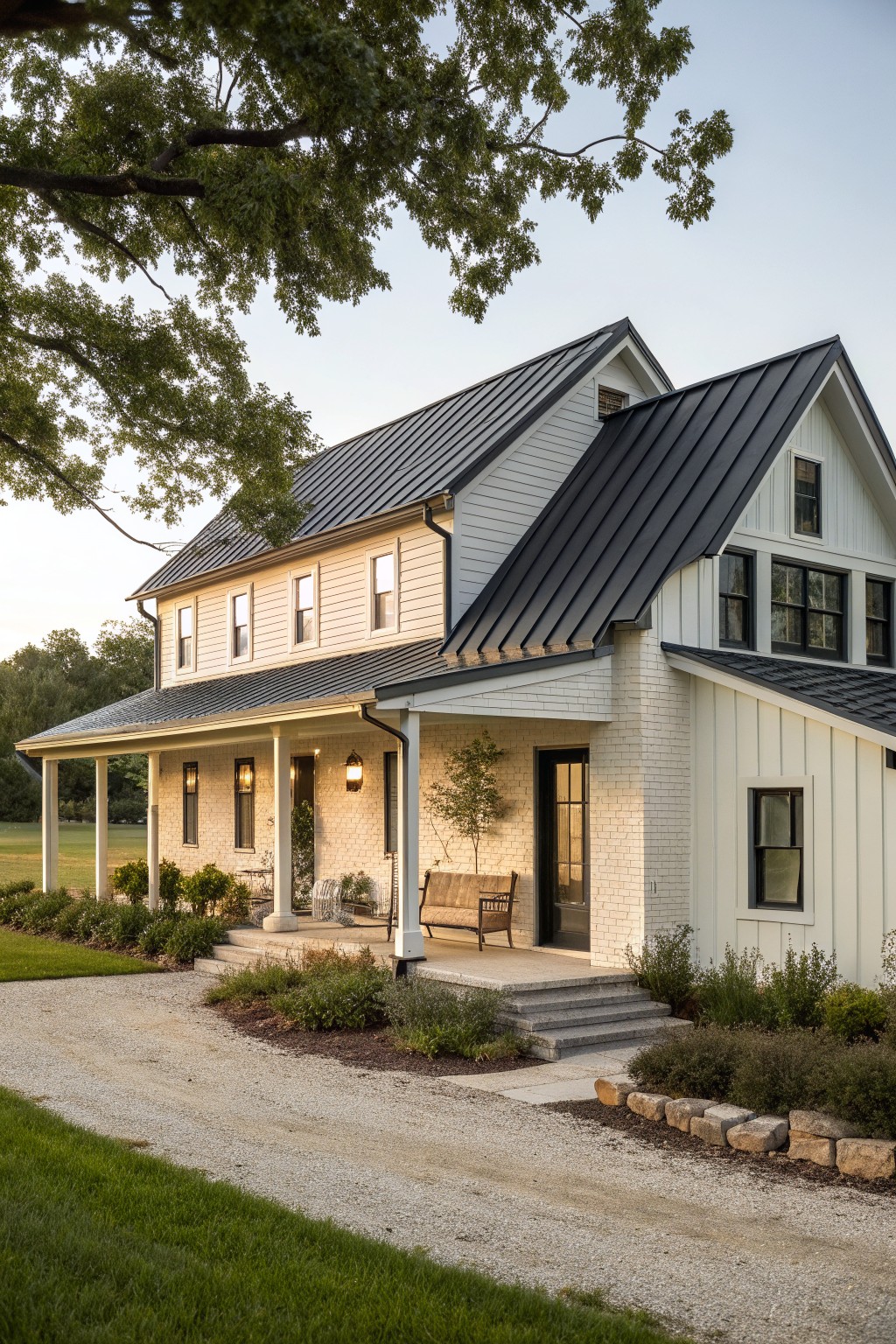 A two-story white farmhouse with brick accents, black metal roofing, a covered porch, and a gravel driveway in front.