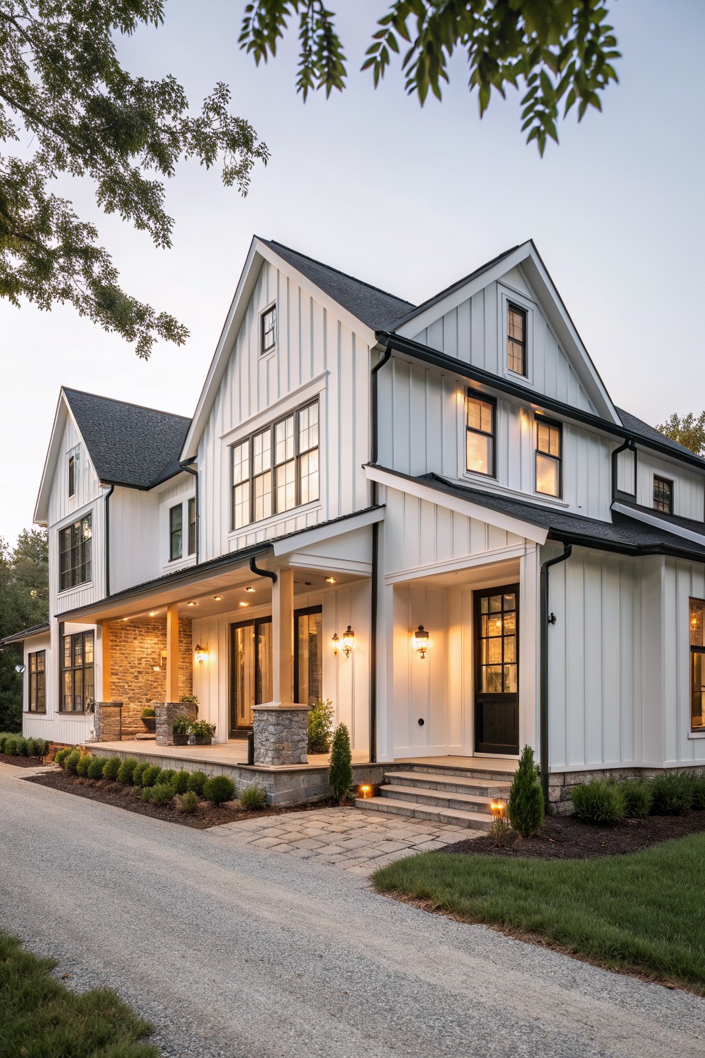 A two-story white farmhouse exterior with multiple large multi-pane windows, a covered porch with stone pillars, and a paved driveway in front.