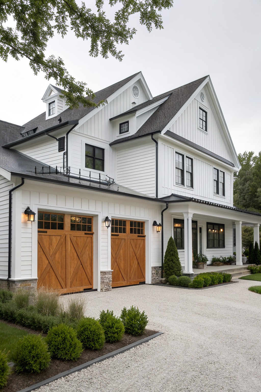 White farmhouse with wooden garage doors, porch, and gravel driveway amid shrubs