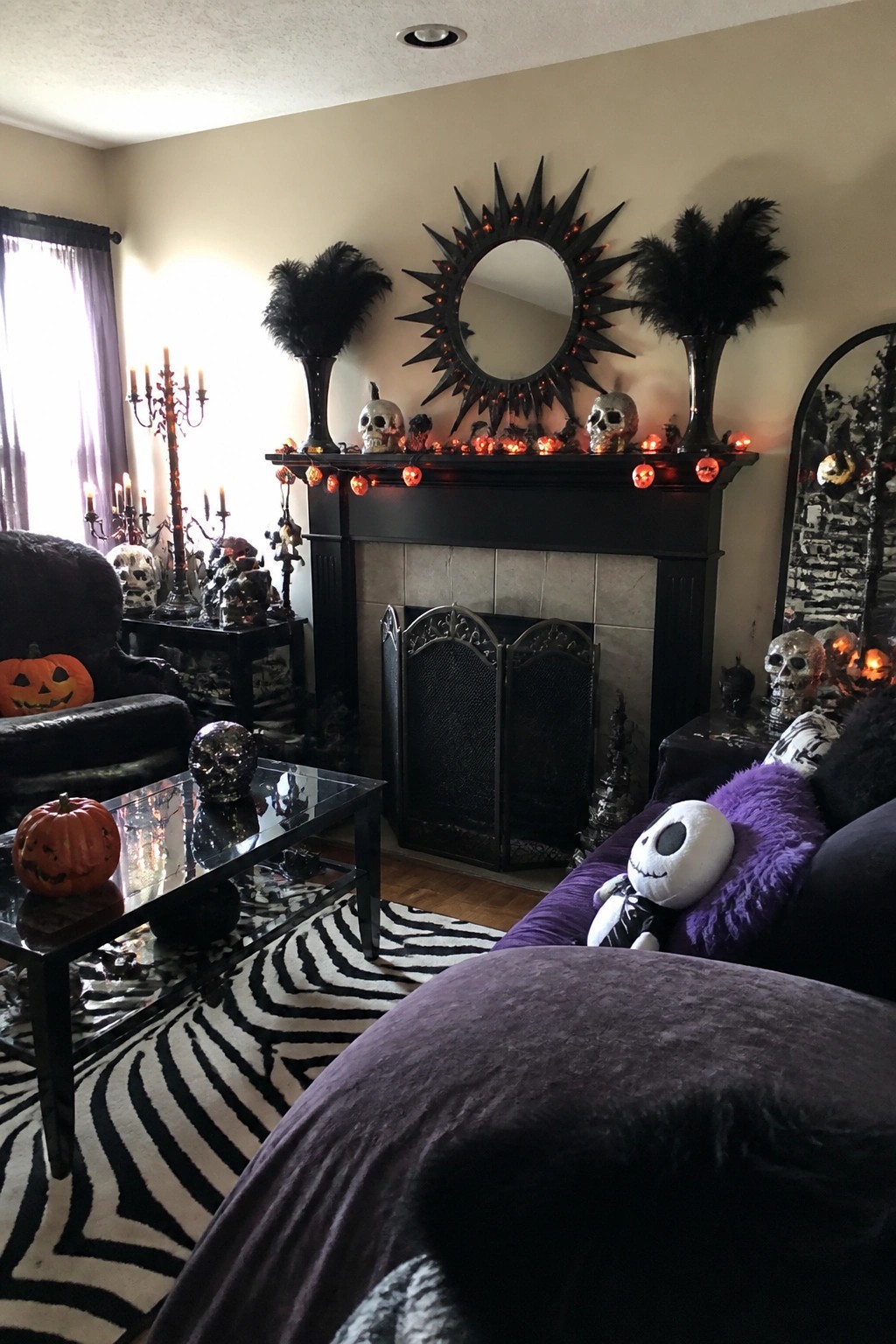 Living room mantel styled for Halloween with skulls, orange string lights, black feather arrangements, and a large sunburst mirror above the fireplace.