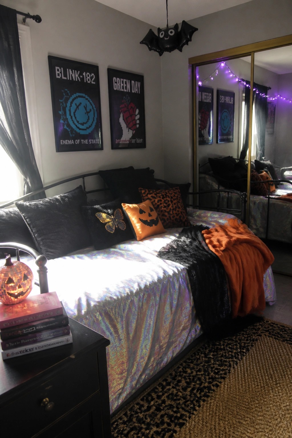 A bedroom with two framed 2000s band posters on the wall above a bed with Halloween-themed pillows and shiny bedding.