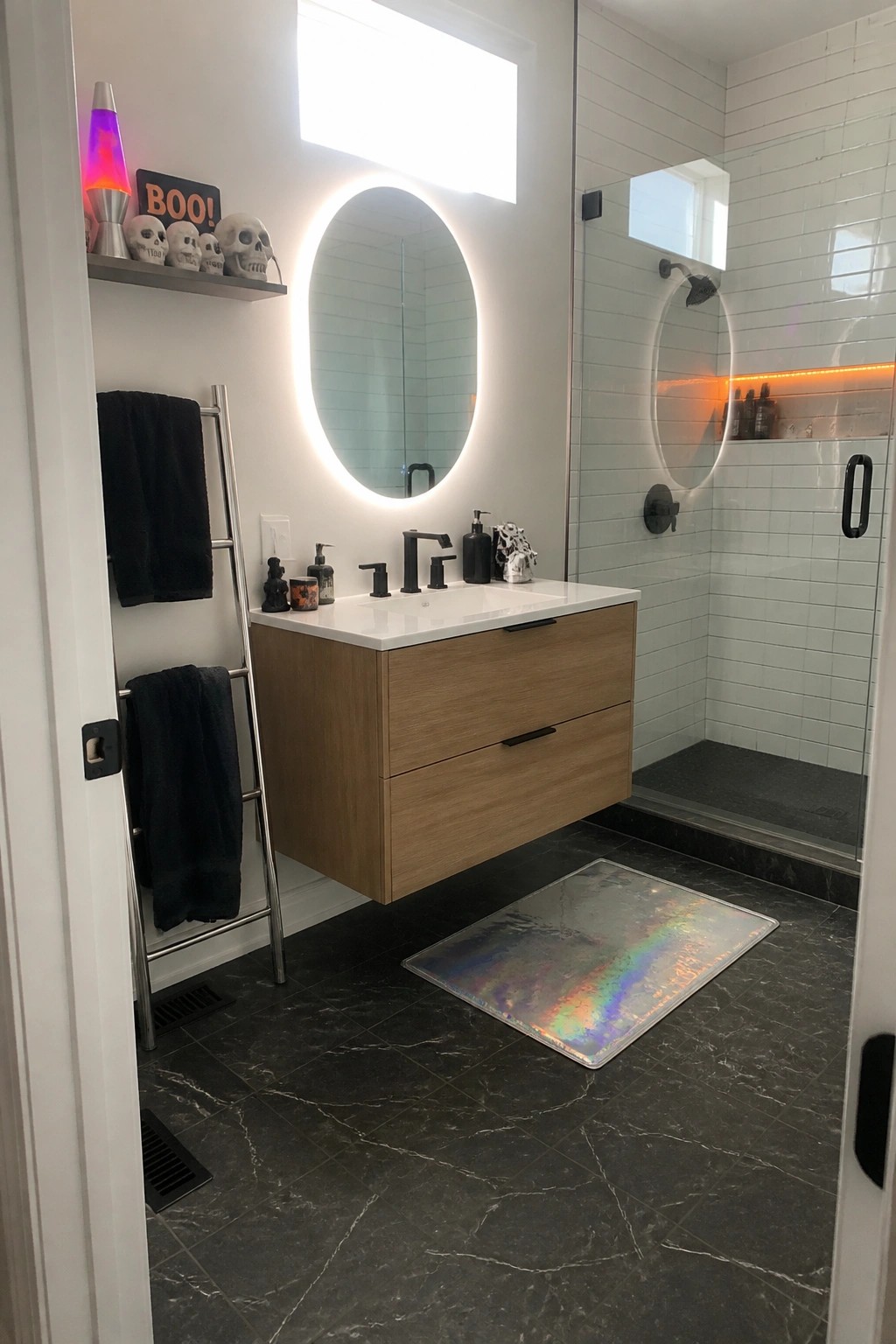 Modern bathroom with floating wood vanity, round lit mirror, black fixtures, and holographic rug