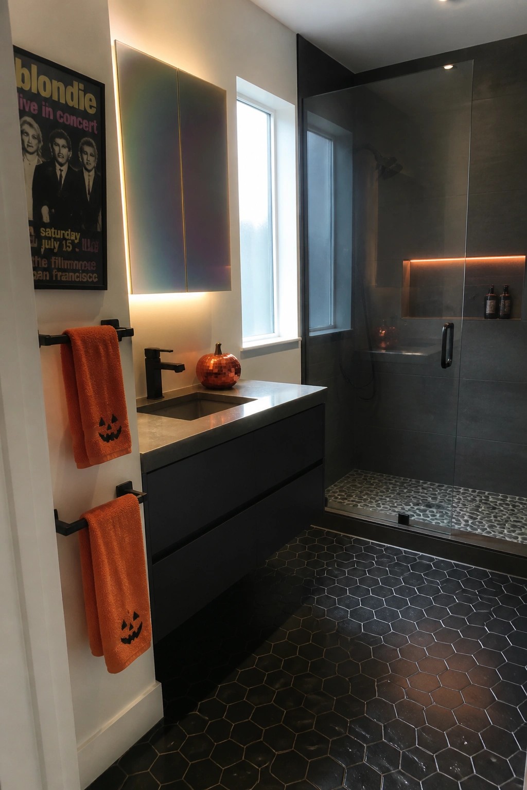 Modern bathroom with black vanity, orange towels featuring jack-o'-lantern faces, and a glass shower enclosure.