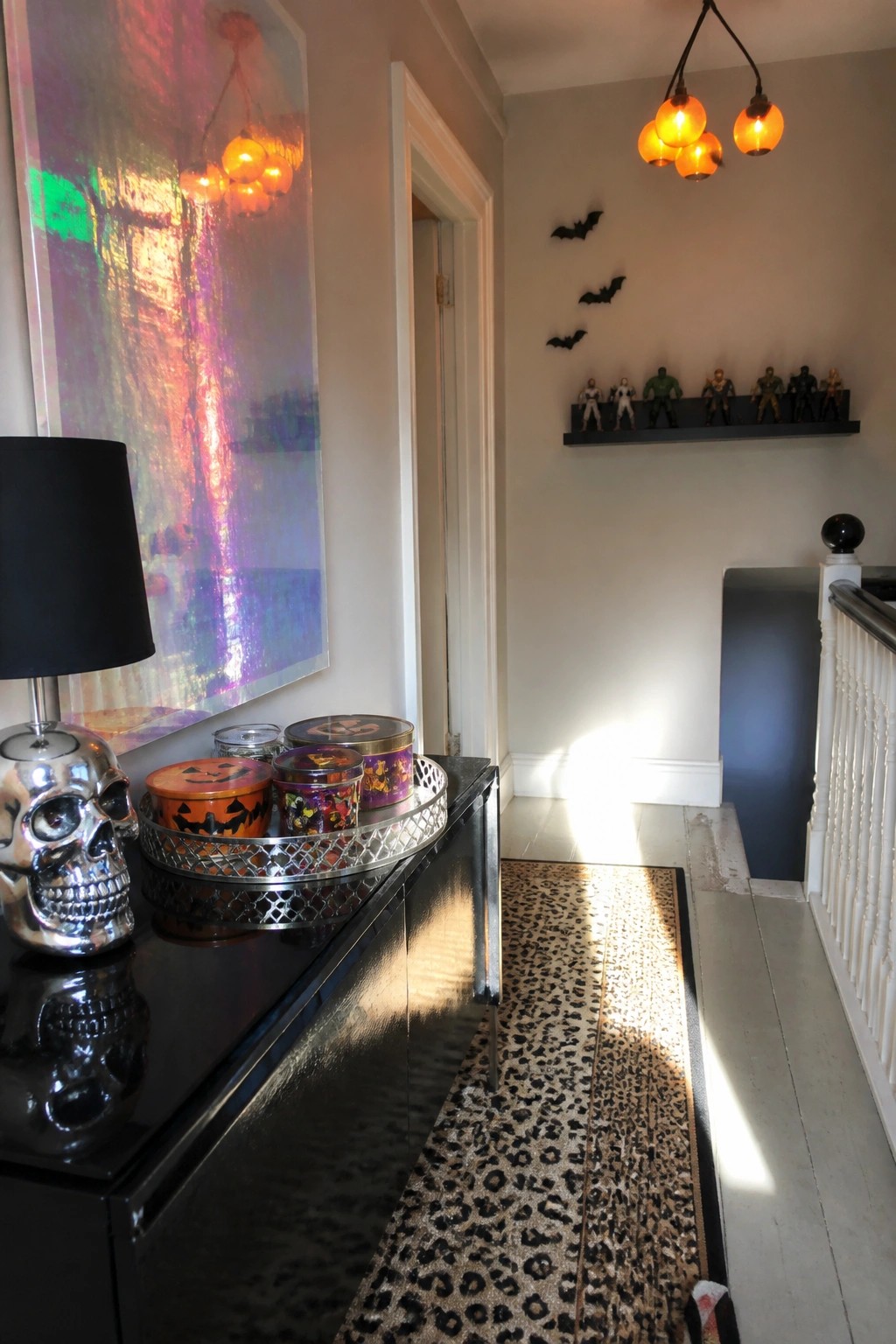 A black console table holds several Halloween-themed tins in a metal tray beside a silver skull lamp, with a leopard-print runner on the floor below.