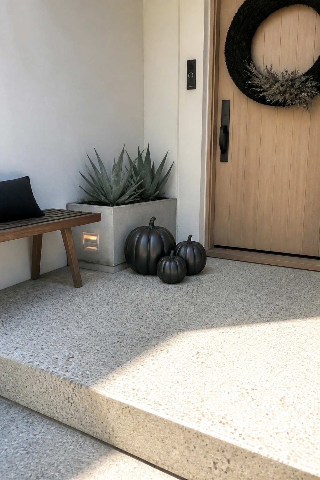 Modern porch with wooden bench, concrete planter, black pumpkins, and wreath on door