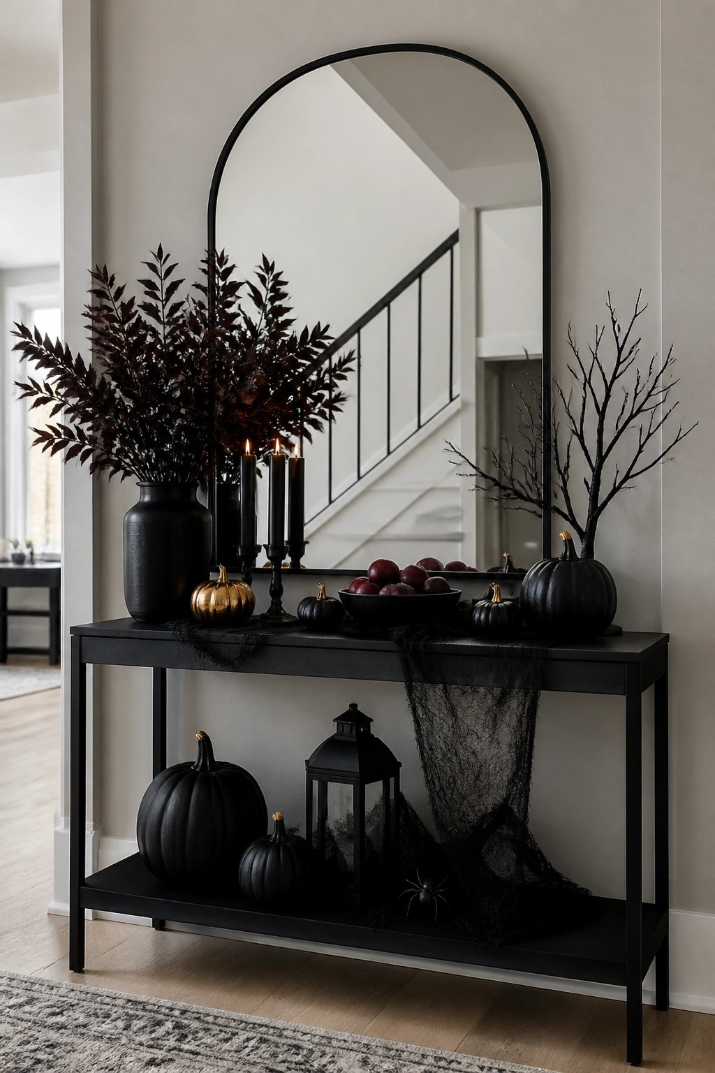 Black console table in an entryway styled with black branches, spiderweb fabric, black pumpkins, and black candles under a large arched mirror.