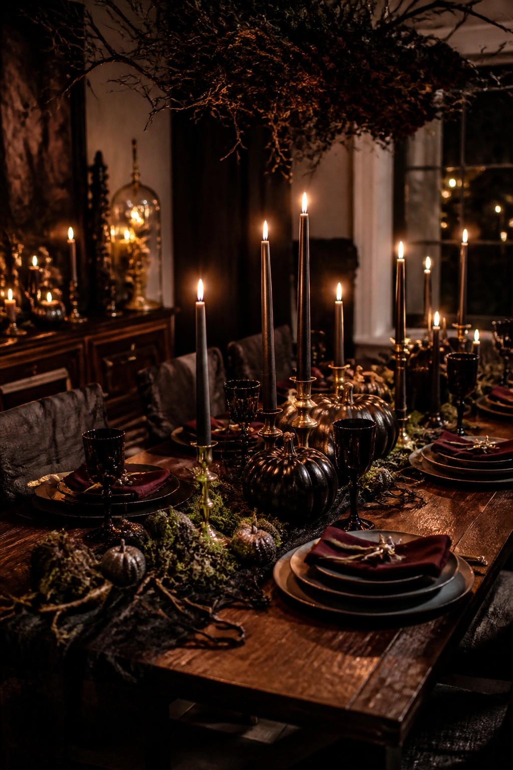 Moody gothic table with lit black candles, metallic pumpkins, moss, and burgundy napkins.