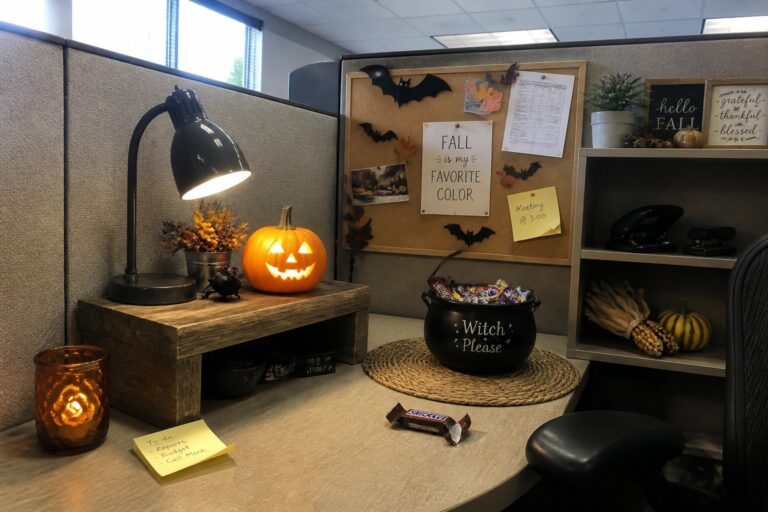 18 Halloween Office Cubicle Decor Ideas That Keep It Festive at Work Office cubicle with glowing jack-o'-lantern, candy cauldron, bat corkboard, and desk.