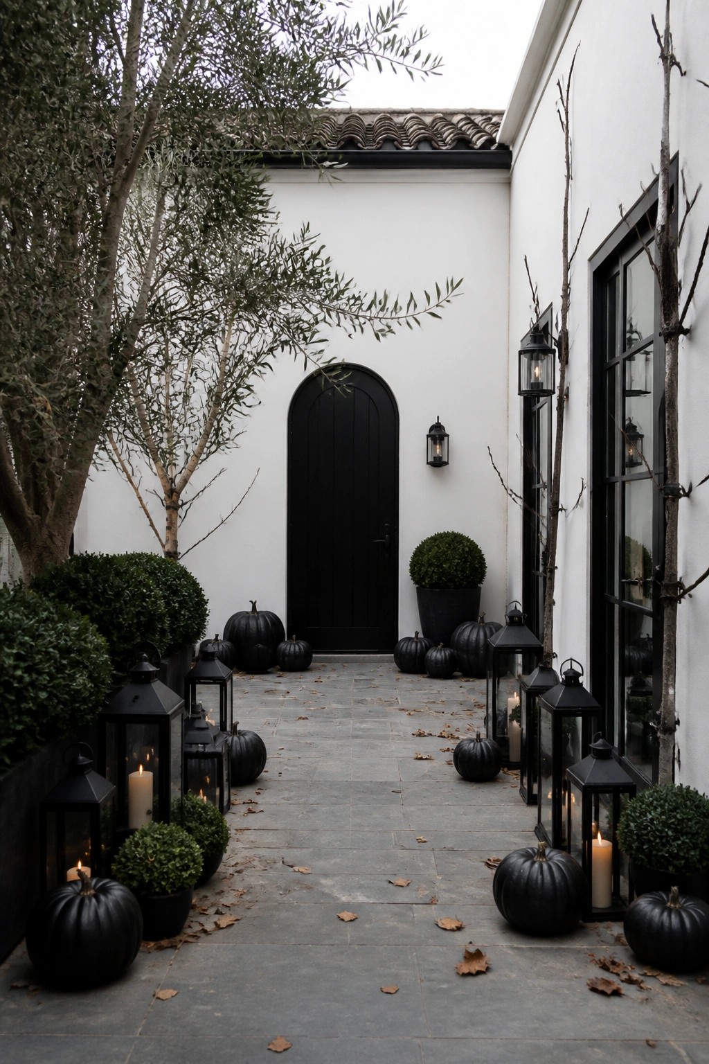 Black pumpkins and glowing lanterns line stone path to arched black door