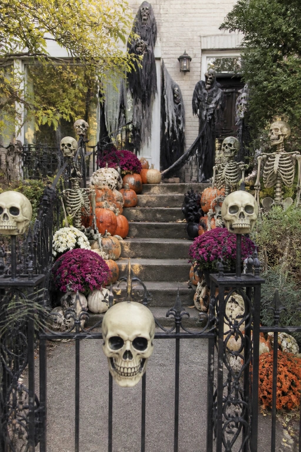 Front entry with multiple plastic skeletons posed on the stairs and fence, skulls mounted on gate posts, and black hanging figures near the door.