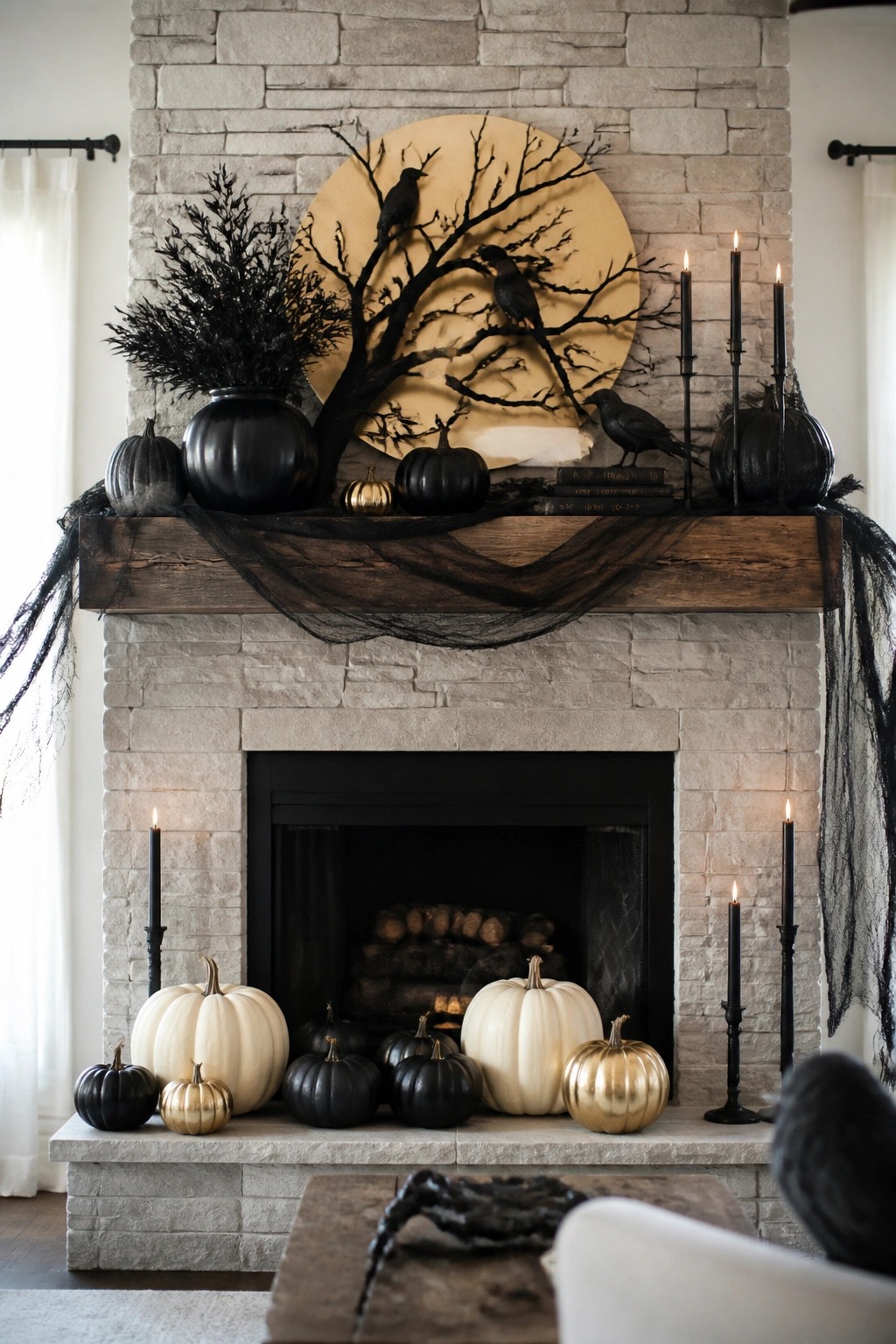 Stone fireplace mantel styled for Halloween with a large circular moon backdrop showing black tree branches and crows, black pumpkins, tall black candles, and dark fabric draped across the mantel.
