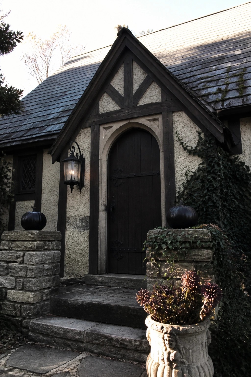 Arched dark wood door on Tudor house with stone steps, black pumpkins, and ivy