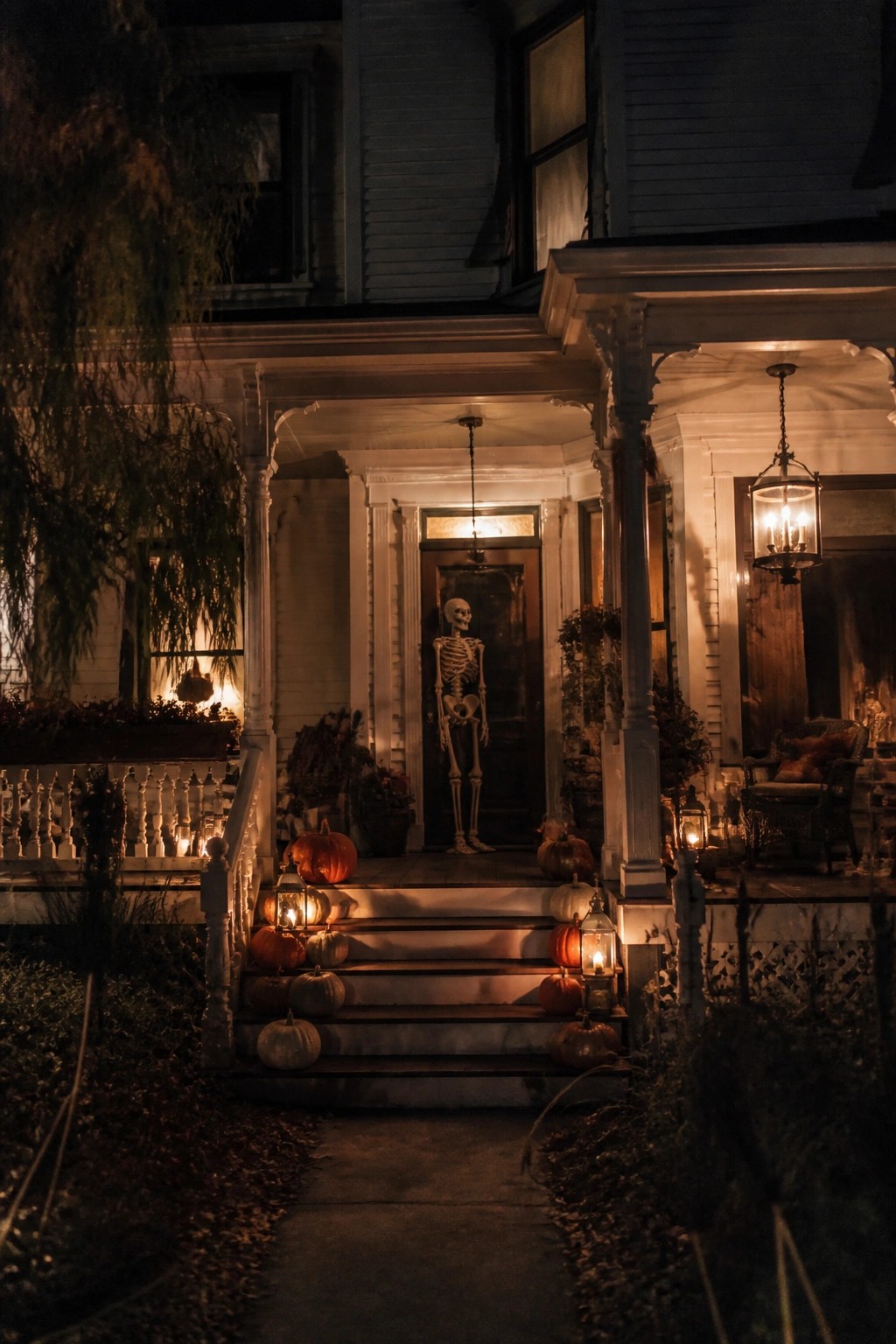 Front porch at night with a skeleton standing in front of the door and pumpkins with lanterns arranged on the steps.