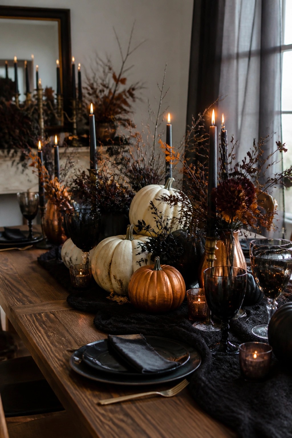 A wooden dining table styled for Halloween with black candles, white and orange pumpkins, dark branches, and black glassware arranged along a dark runner.