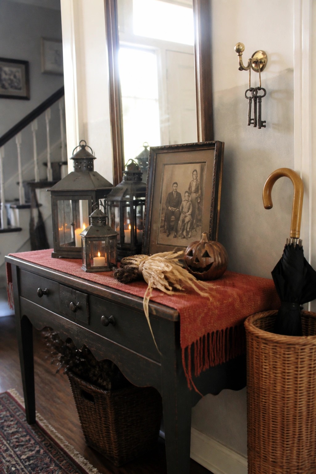 A dark wood console table with metal lanterns, a framed vintage photo, a carved pumpkin, and dried corn on a red runner.