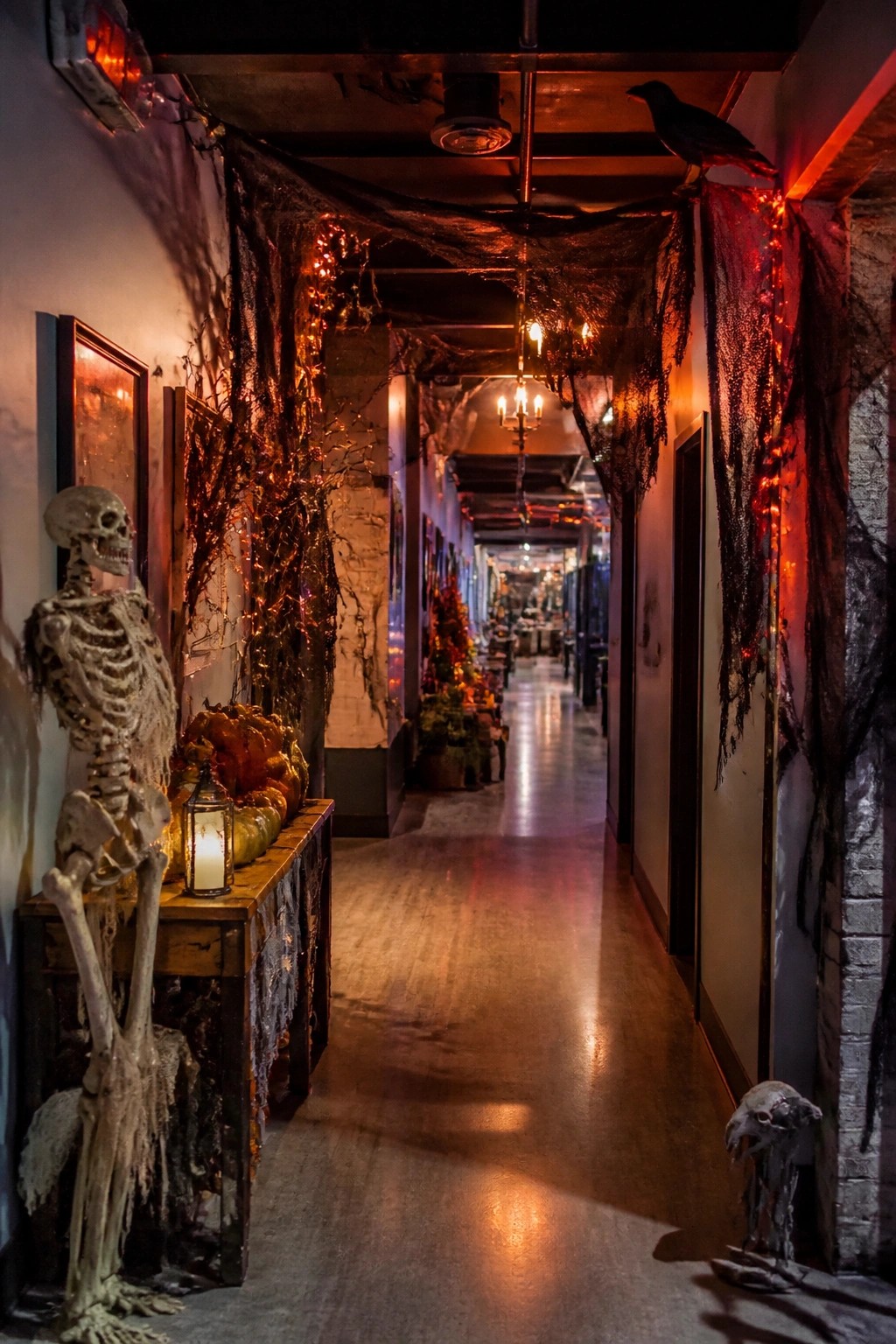 Halloween hallway with skeleton, pumpkins, crow, spiderwebs, and glowing orange lights.