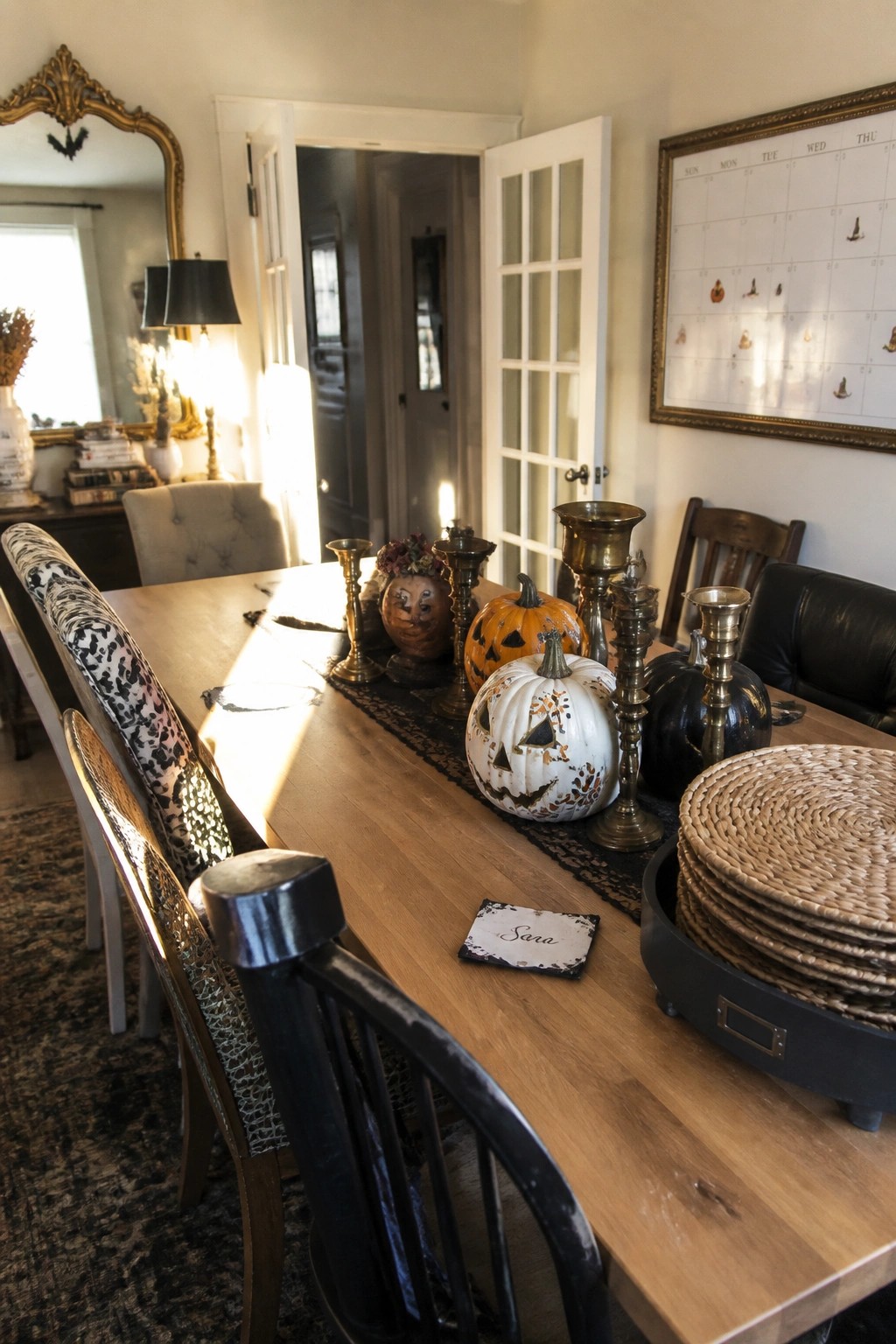 Wooden dining table with carved pumpkins, brass candlesticks, black runner, and woven placemats