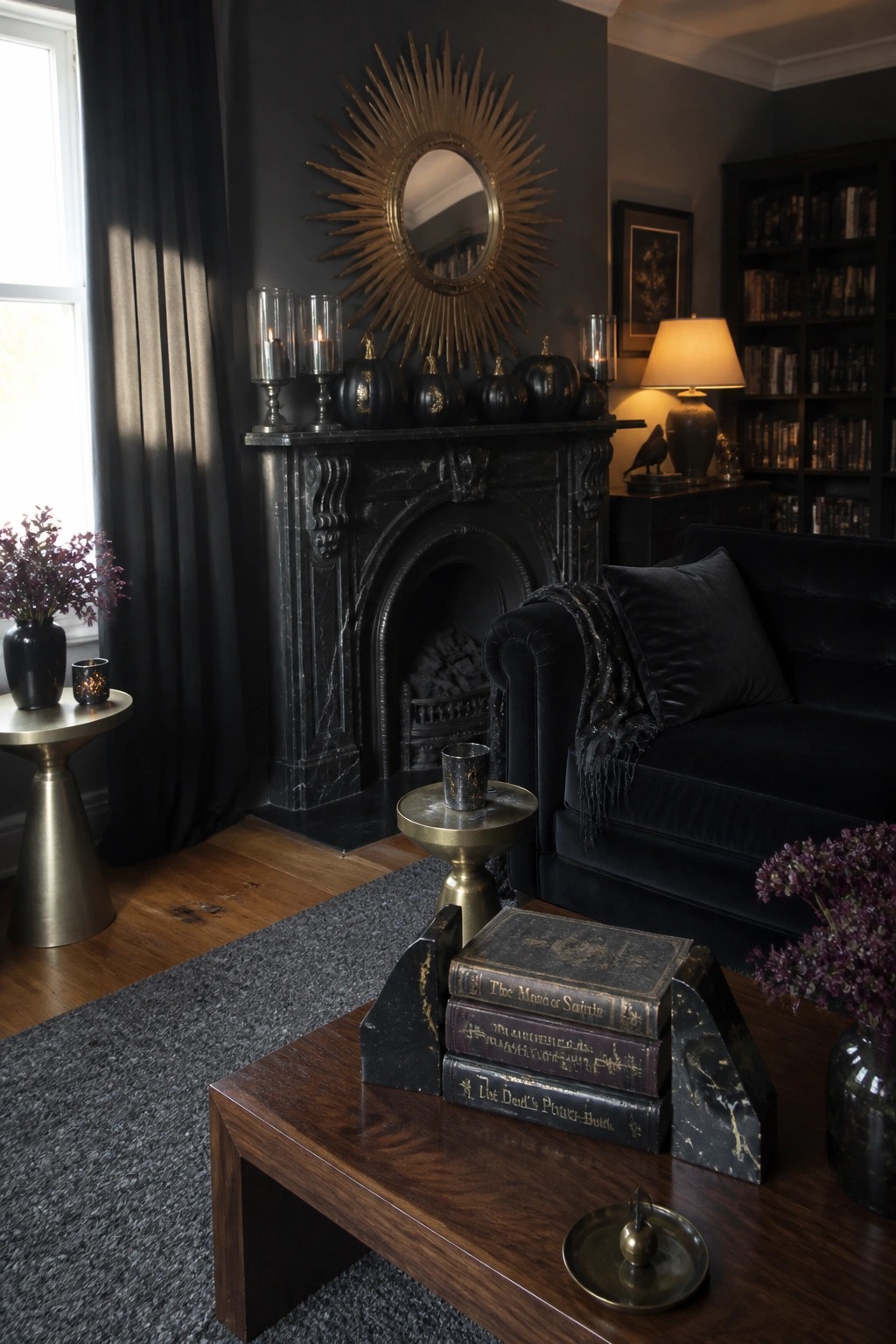 A dark living room features a black marble fireplace mantel lined with black pumpkins, lit candles, and a large gold sunburst mirror above it, next to a black velvet sofa.