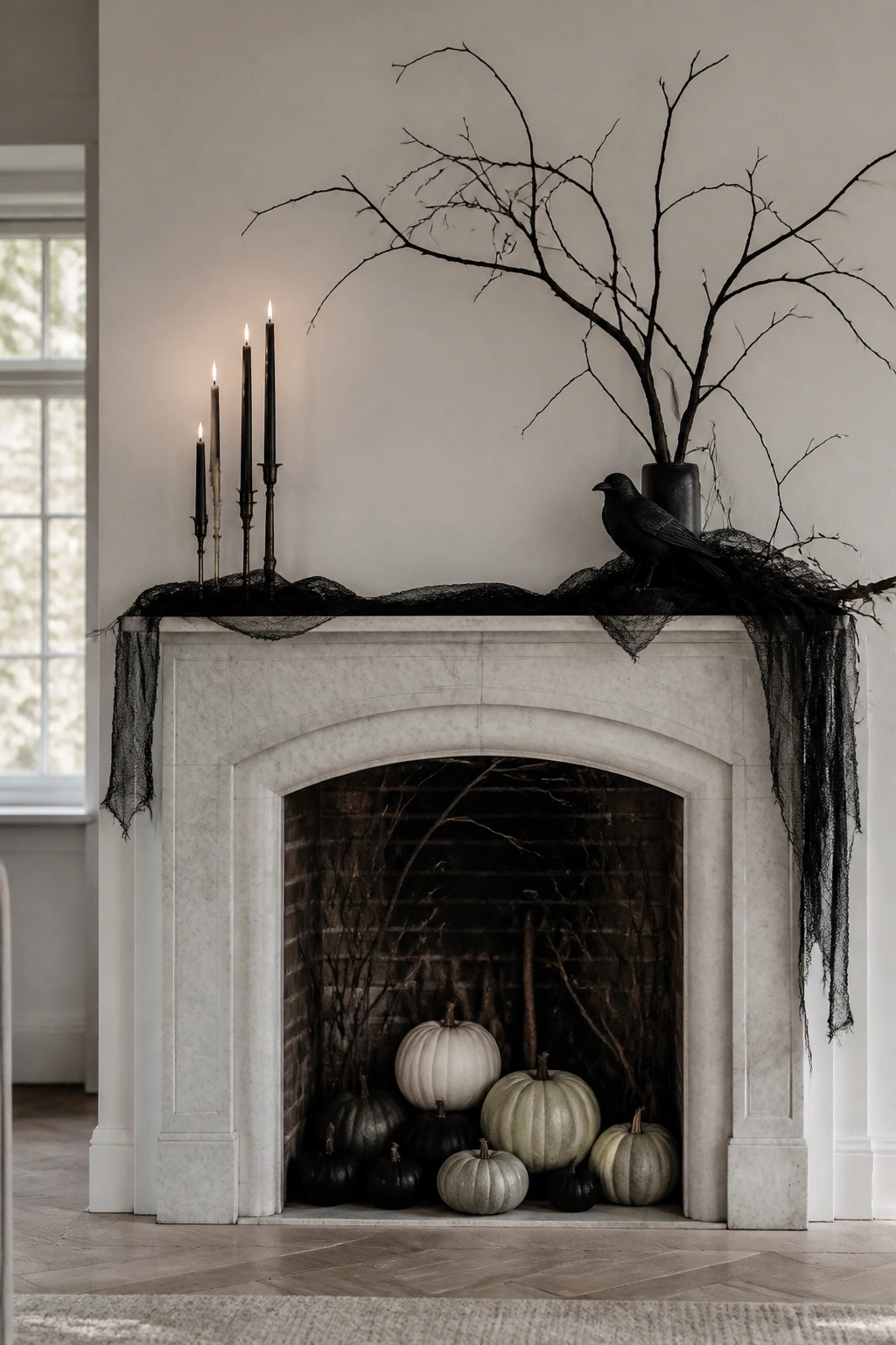 White marble fireplace with black branches in a vase, a black crow perched on the mantel, black candles, and sheer black fabric draped across the top, plus assorted pumpkins in the hearth.