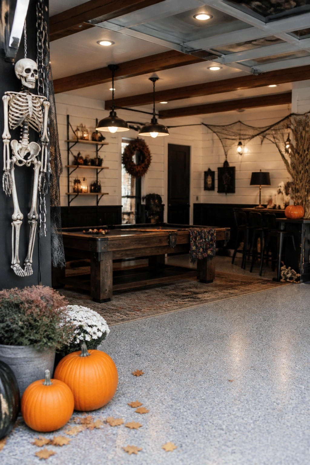 Garage game room with a large skeleton chained to the wall beside a pool table, spiderwebs, and pumpkins on the floor.
