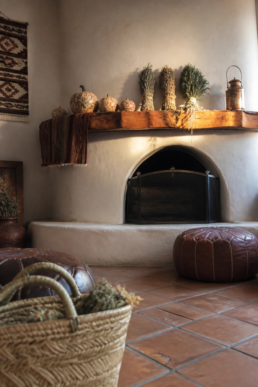 A white plaster fireplace with a thick wooden mantle holding small decorative gourds, bundles of dried herbs, and a metal lantern above an arched firebox.