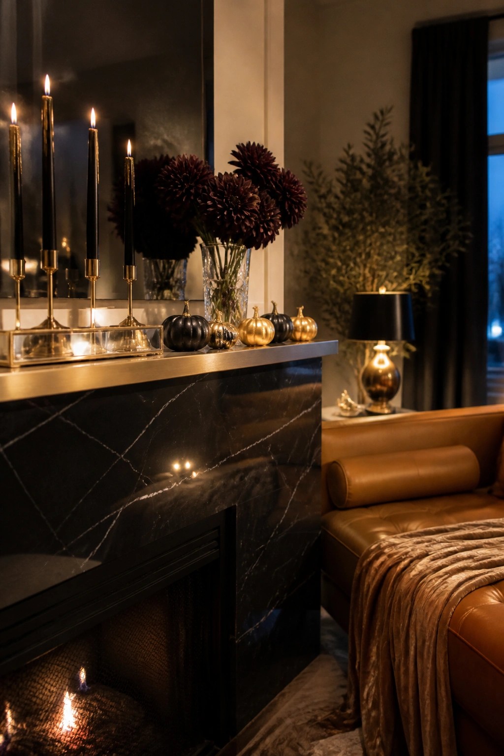 Black marble fireplace with lit candles, dark dahlias, gold pumpkins beside leather sofa.