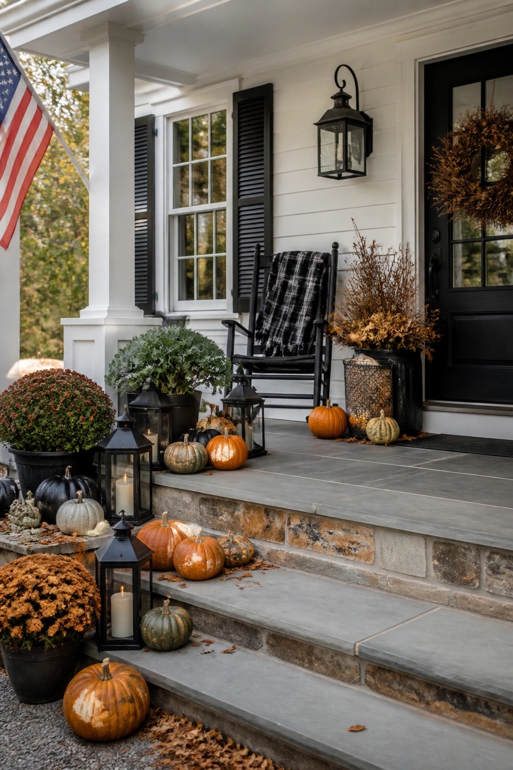 Farmhouse front porch with pumpkins of various sizes placed along the stone steps and around potted mums and lanterns.