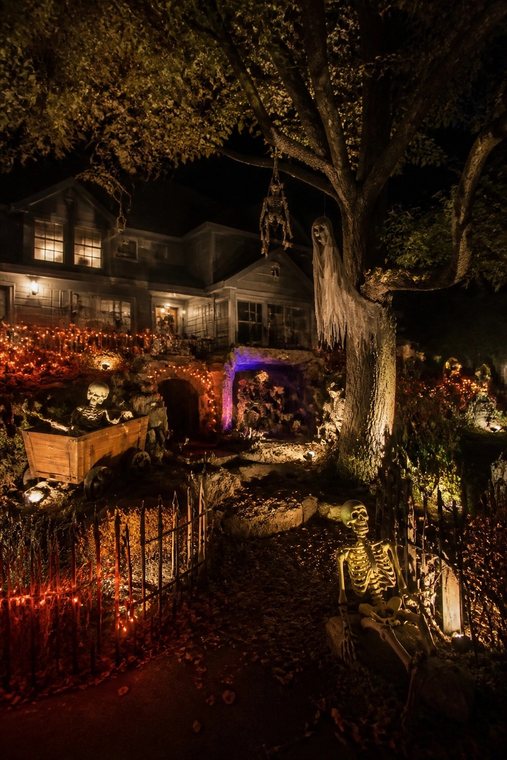 Spooky skeletons, red lights, and hanging figures decorate a dark house at night.