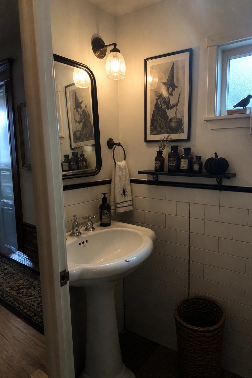 A bathroom with white subway tile, a pedestal sink, two framed vintage witch prints on the walls, and a black shelf holding brown bottles and a pumpkin.