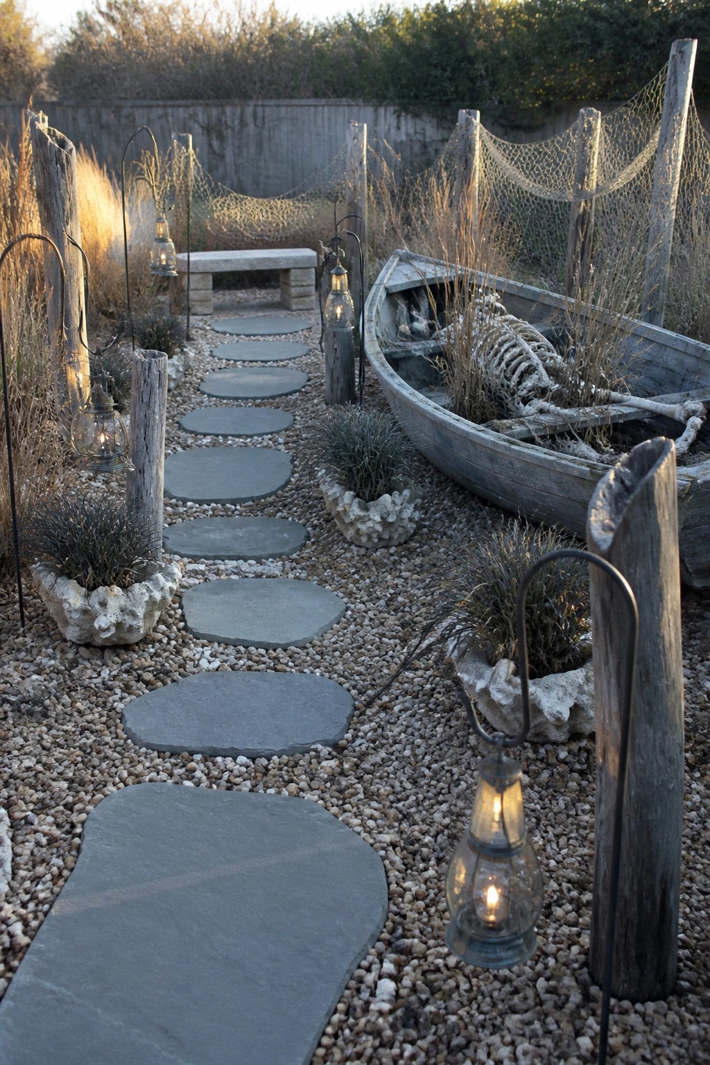 A gravel path with irregular gray stepping stones runs through a garden, flanked by hanging lanterns on wooden posts, fishing nets, and a weathered boat holding a skeleton.