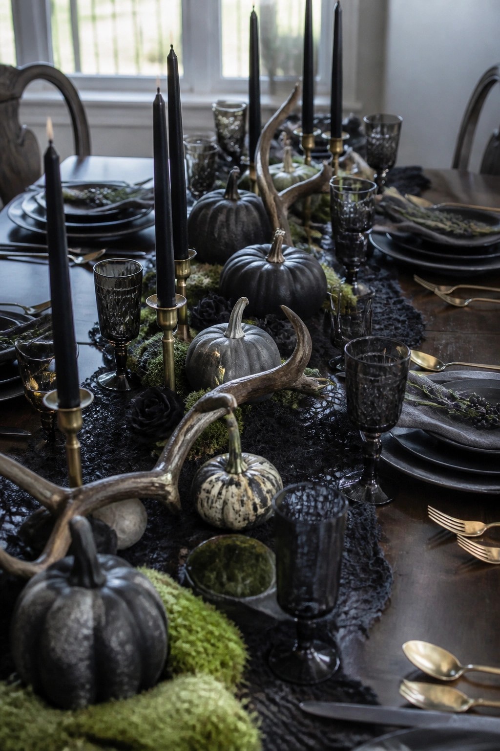 Dark wooden dining table set with black pumpkins, tall black candles, antlers, moss, and black glassware for a Halloween tablescape.