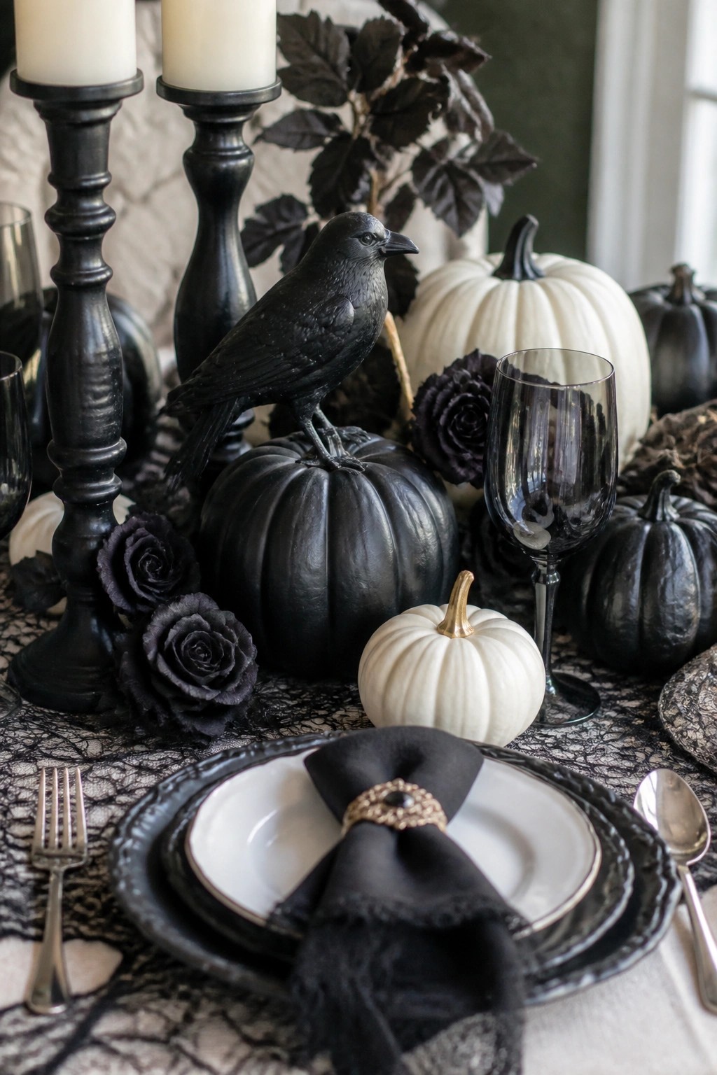 A formal dining table decorated for Halloween with a black crow figurine on a black pumpkin, surrounded by white and black pumpkins, dark roses, black candles, and black place settings.