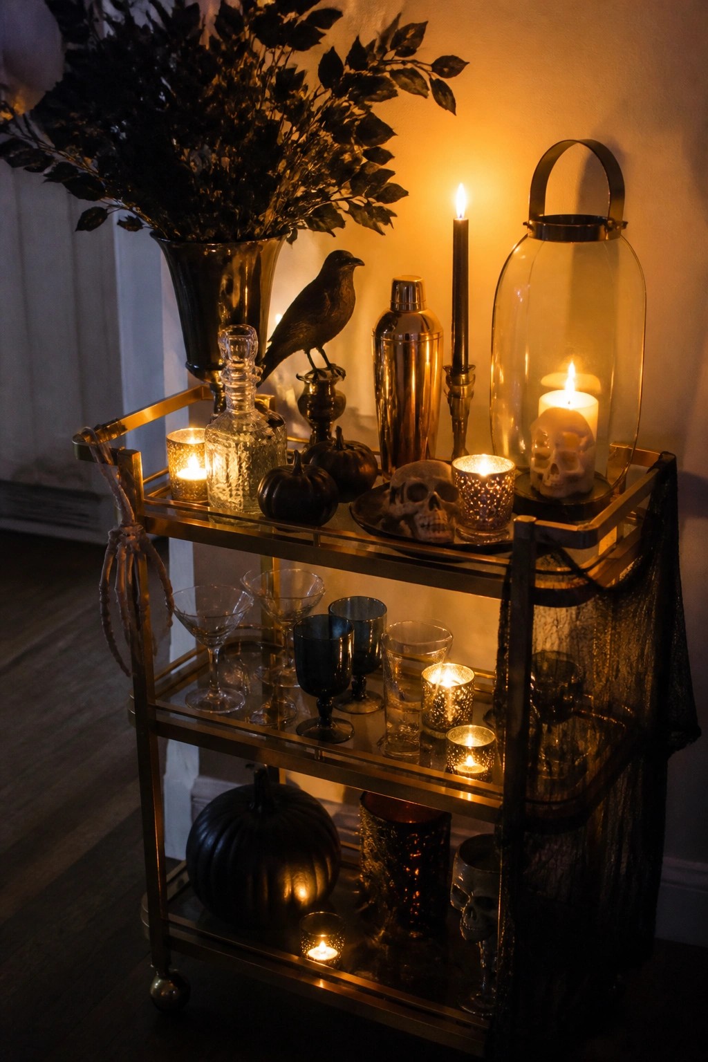 Gold bar cart with black pumpkins, skulls, lit candles, and glassware in warm light.