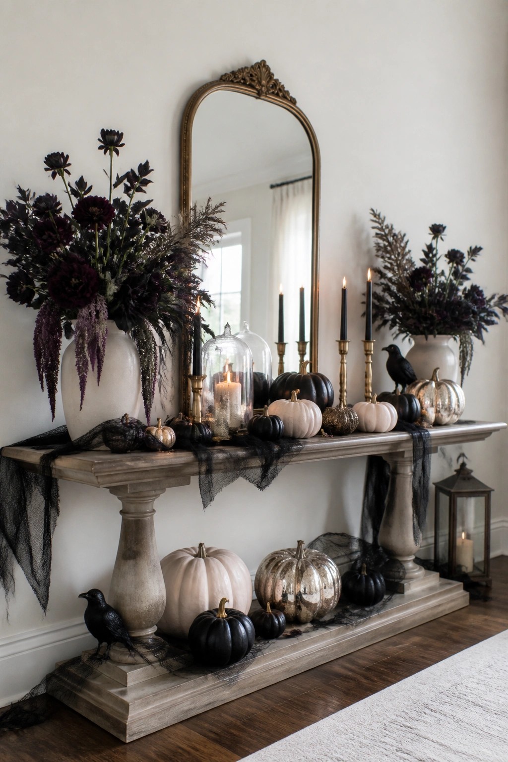 Elegant console table with black, white, and metallic pumpkins, lit candles, dark flowers, and crows.
