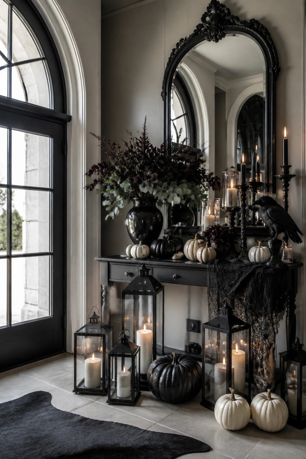 Entryway console styled with black and white pumpkins, black lanterns, a crow figure, dark foliage, and spiderweb fabric under an ornate black mirror.
