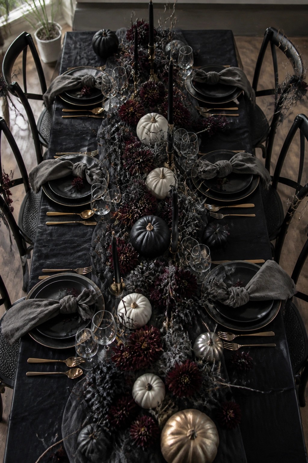 A long dining table covered in a black runner with black candles, assorted pumpkins, and dark flowers running down the center.