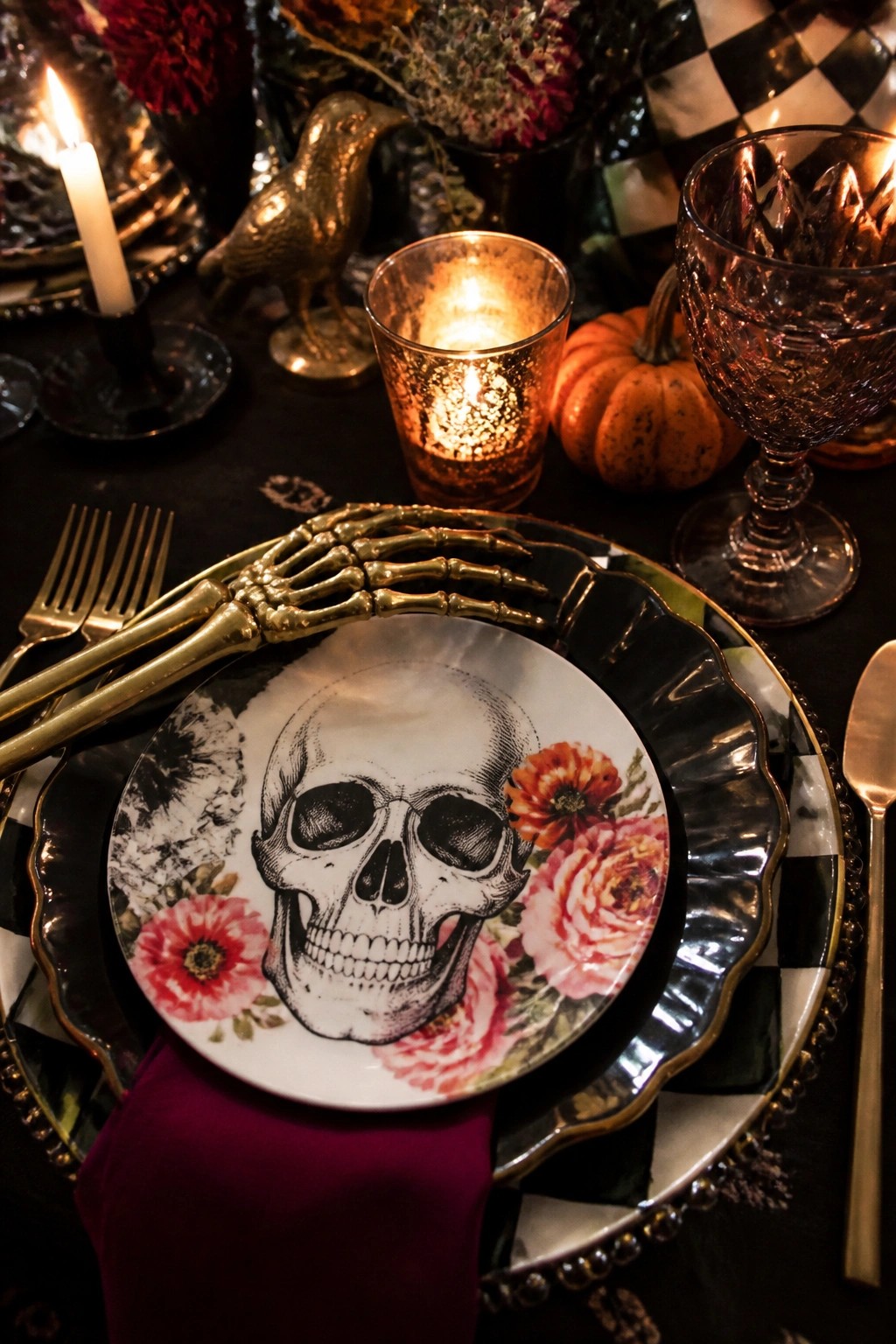 Close-up of a Halloween tablescape with a white skull and floral plate, golden skeleton hand cutlery, and dark checkered charger on a black table.