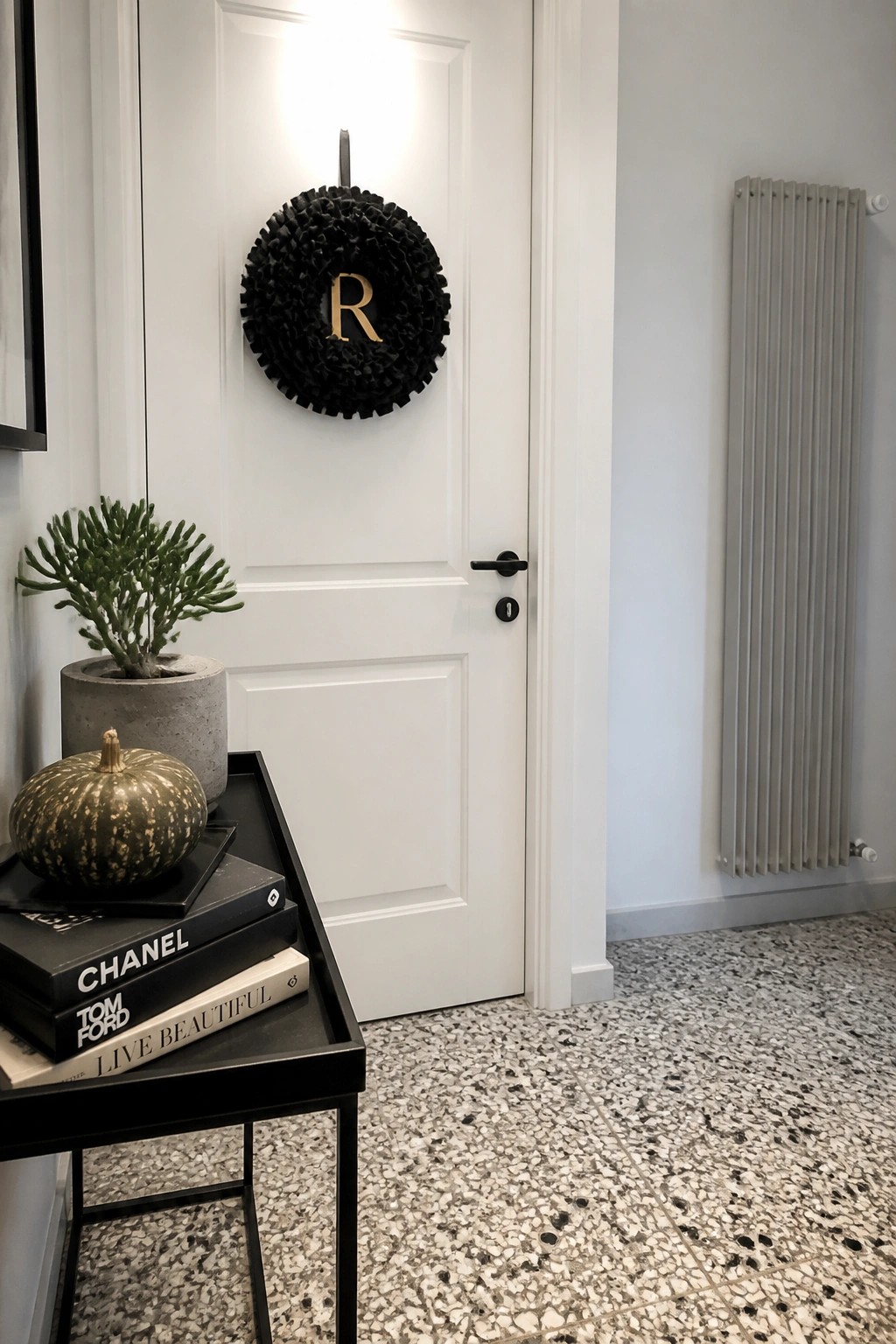 White door with black wreath beside console table holding books, plant, and pumpkin on terrazzo floor